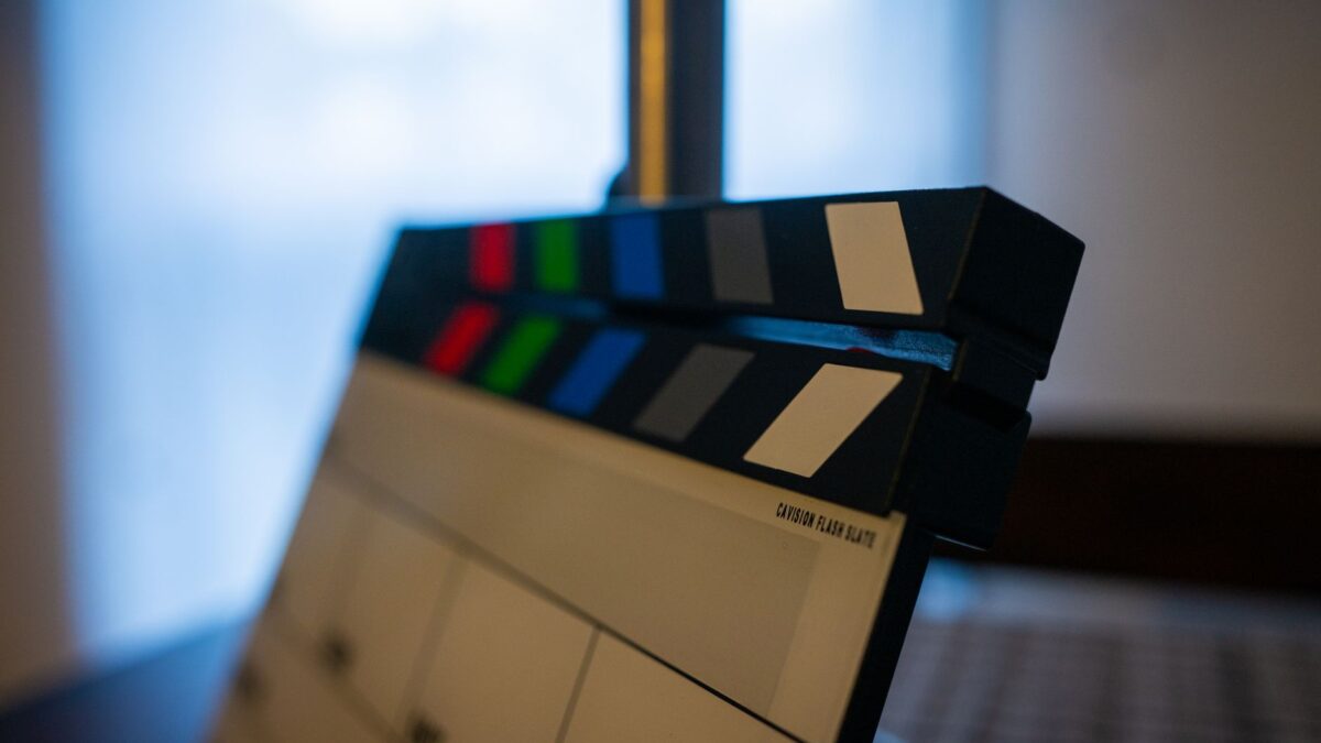Clapă de film alb-negru cu benzi colorate roșii, verzi, albastre și gri, în prim-plan, așezată în fața unei ferestre estompate cu lumină albăstruie.